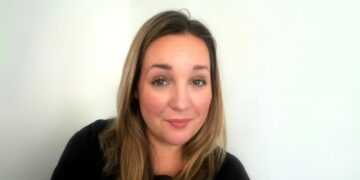 A headshot of a woman with dark blonde hair, wearing a black top.