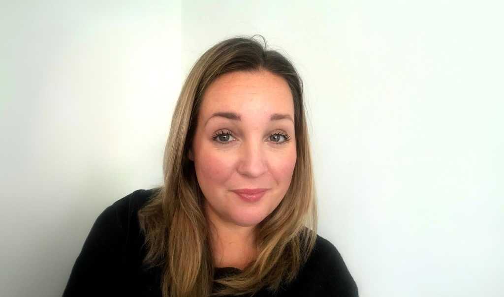 A headshot of a woman with dark blonde hair, wearing a black top.